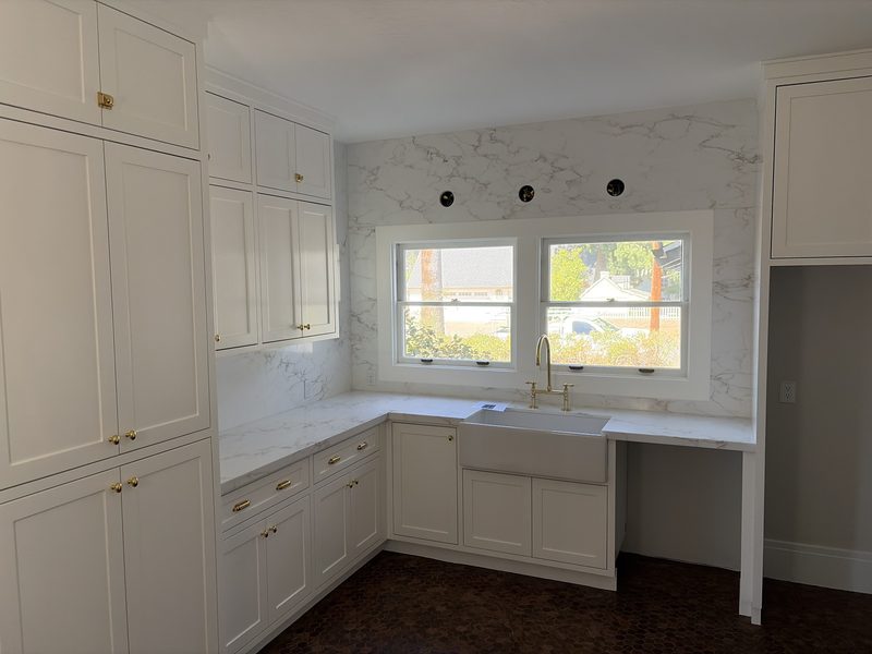White L-shaped kitchen with a farmhouse sink under two windows and white quartz counters and backsplash