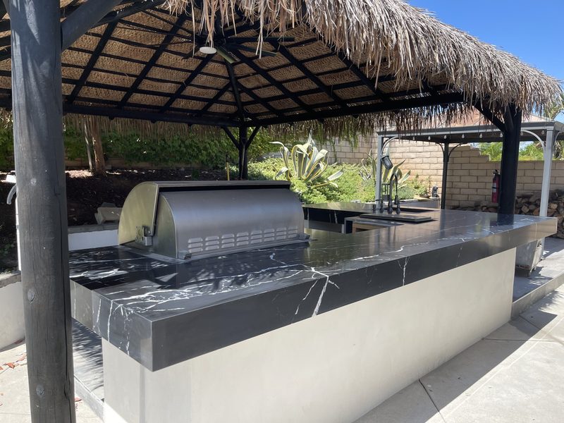 Outdoor kitchen under a palapa with a black quartz countertop and built-in grill