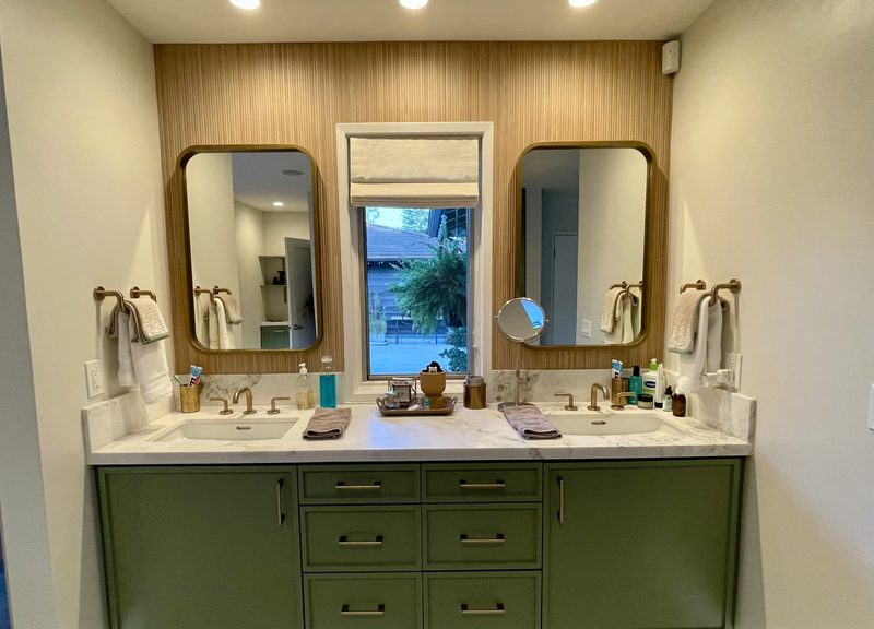Double vanity in sage green with a marble top, two brass-framed mirrors and a white oak wall